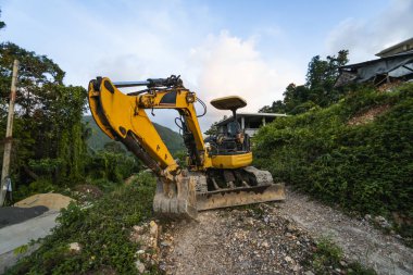 Günbatımında gökyüzü olan modern kazı alanı. Geniş çaplı bir kazı aracı yeşil çimlerle kaplı bir tepede duruyordu. Kırsal kesimde yeni bir bina inşa etmek için makineler.