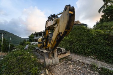 Günbatımında gökyüzü olan modern kazı alanı. Geniş çaplı bir kazı aracı yeşil çimlerle kaplı bir tepede duruyordu. Kırsal kesimde yeni bir bina inşa etmek için makineler.