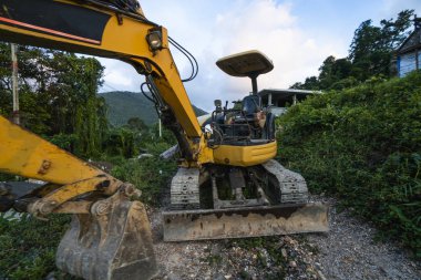Günbatımında gökyüzü olan modern kazı alanı. Geniş çaplı bir kazı aracı yeşil çimlerle kaplı bir tepede duruyordu. Kırsal kesimde yeni bir bina inşa etmek için makineler.