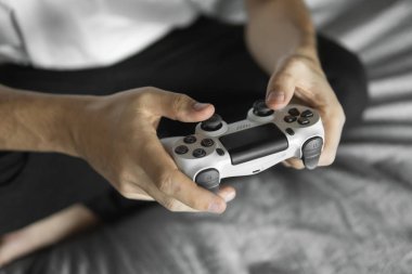 Beyaz tişörtlü bir oyuncu elinde bir av tüfeği tutuyor ve bir kanepede oturuyor. Adam elleri beyaz bir kumandayla video oyunu oynuyor. Evde zevkle bir video oyunu oynayın..