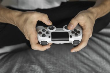 Beyaz tişörtlü bir oyuncu elinde bir av tüfeği tutuyor ve bir kanepede oturuyor. Adam elleri beyaz bir kumandayla video oyunu oynuyor. Evde zevkle bir video oyunu oynayın..