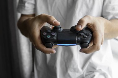 Beyaz tişörtlü bir oyuncu elinde bir av sahası tutuyor. Adam elleri siyah bir kontrolörle video oyunu oynuyor. Evde zevkle bir video oyunu oynayın..