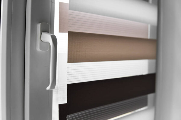 Окно ручки и белый ролик ткани жалюзи на белом пластиковом окне в гостиной. Закрыть шторы в помещении
.