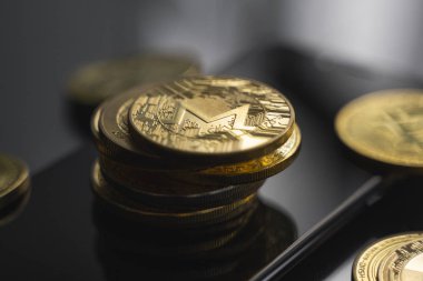 Masasında bir sürü bitcoin olan akıllı bir telefonun üzerinde altın Monero bitcoin yığını. Sanal kripto para birimi kavramı. Sanal para madenciliği çevrimiçi işyeri. Bitcoin ticareti.