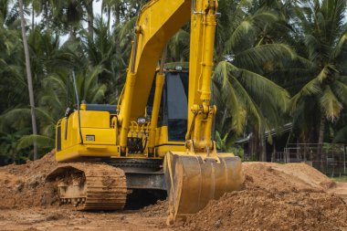 Mavi gökyüzüne karşı bir inşaat alanında sarı kazıcı. Ağır endüstri. Endüstriyel kazıcının detaylarını kapat. Arka planda avuç içleri olan turuncu bir zeminde duran büyük bir iz kazıcı..