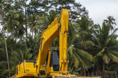 Mavi gökyüzüne karşı bir inşaat alanında sarı kazıcı. Ağır endüstri. Endüstriyel kazıcının detaylarını kapat. Arka planda avuç içleri olan turuncu bir zeminde duran büyük bir iz kazıcı..