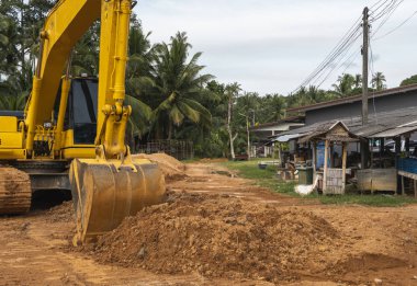 Mavi gökyüzüne karşı bir inşaat alanında sarı kazıcı. Ağır endüstri. Endüstriyel kazıcının detaylarını kapat. Arka planda avuç içleri olan turuncu bir zeminde duran büyük bir iz kazıcı..