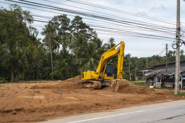 Mavi gökyüzüne karşı bir inşaat alanında sarı kazıcı. Ağır endüstri. Endüstriyel kazıcının detaylarını kapat. Arka planda avuç içleri olan turuncu bir zeminde duran büyük bir iz kazıcı..