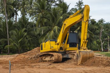 Mavi gökyüzüne karşı bir inşaat alanında sarı kazıcı. Ağır endüstri. Endüstriyel kazıcının detaylarını kapat. Arka planda avuç içleri olan turuncu bir zeminde duran büyük bir iz kazıcı..