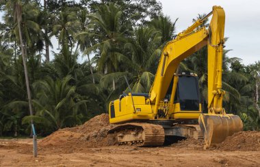 Mavi gökyüzüne karşı bir inşaat alanında sarı kazıcı. Ağır endüstri. Endüstriyel kazıcının detaylarını kapat. Arka planda avuç içleri olan turuncu bir zeminde duran büyük bir iz kazıcı..