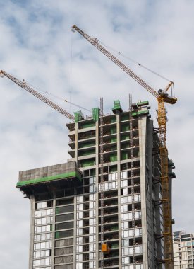 Mavi gökyüzüne karşı vinçleri olan yüksek katlı bir bina inşa etme şantiyesi.