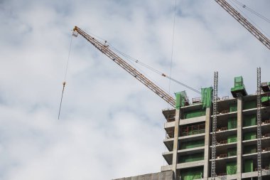 Mavi gökyüzüne karşı vinçleri olan yüksek katlı bir bina inşa etme şantiyesi.