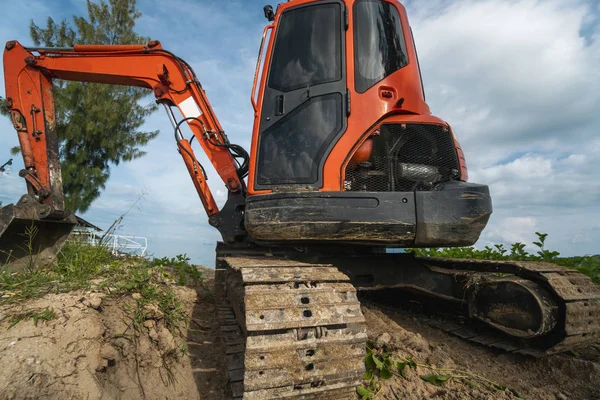 Small orange excavator on a ground against blue sky and sea for a works on construction site. Small tracked excavator standing on a ground with a blue sea on background. Heavy industry. — 图库照片