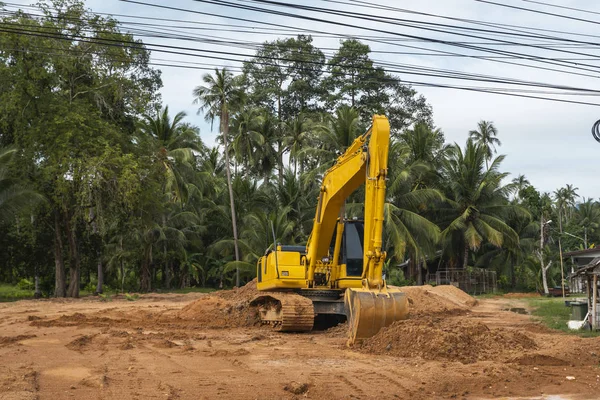 Mavi gökyüzüne karşı bir inşaat alanında sarı kazıcı. Ağır endüstri. Endüstriyel kazıcının detaylarını kapat. Arka planda avuç içleri olan turuncu bir zeminde duran büyük bir iz kazıcı..