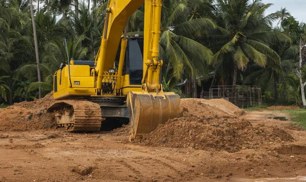 Mavi gökyüzüne karşı bir inşaat alanında sarı kazıcı. Ağır endüstri. Endüstriyel kazıcının detaylarını kapat. Arka planda avuç içleri olan turuncu bir zeminde duran büyük bir iz kazıcı..