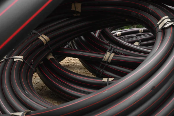 Rury z czarnej gumy lub tworzywa sztucznego z czerwonymi liniami jako materiałem budowlanym i wyposażeniem na placu budowy. Użycie jako rury wodnej. — Zdjęcie stockowe