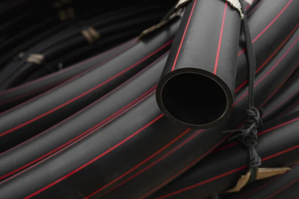 Fekete gumi vagy műanyag csövek piros vonalakkal, mint építőanyag és felszerelés az építési területen. Vízvezetékként való használat. — Stock Fotó