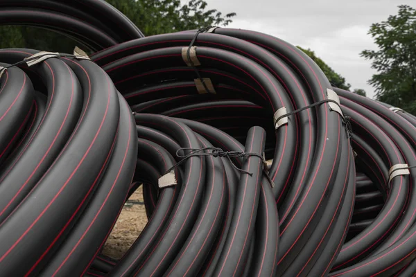 Schwarze Gummi- oder Kunststoffrohre mit roten Linien als Baumaterial und Ausrüstung auf der Baustelle. Verwendung als Wasserleitung. — Stockfoto