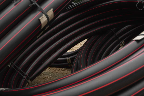 Fekete gumi vagy műanyag csövek piros vonalakkal, mint építőanyag és felszerelés az építési területen. Vízvezetékként való használat. — Stock Fotó