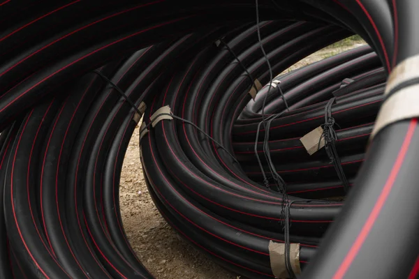 Tubi di gomma o plastica nera con linee rosse come materiale da costruzione e attrezzature in cantiere. Utilizzo come tubo dell'acqua . — Foto Stock