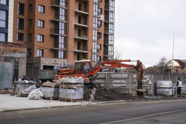Turuncu kazıcı bir çakılla inşaat alanında çalışır ve onu bir yerden başka bir yere taşır. Ağır endüstri. Bir binanın inşaatı.