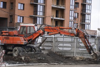 Turuncu kazıcı bir çakılla inşaat alanında çalışır ve onu bir yerden başka bir yere taşır. Ağır endüstri. Bir binanın inşaatı.