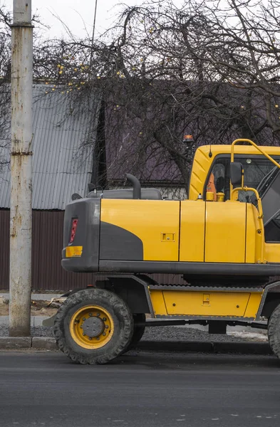 Желтый экскаватор стоит на дороге на строительной площадке дороги на улице. Тяжелая промышленность. Строительство дороги. — стоковое фото