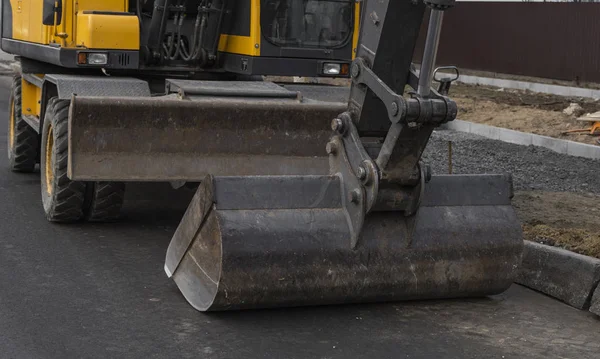 Yellow excavator standing on a road on construction site of the road on a street. Heavy industry. Construction of a road. — Stock Photo, Image