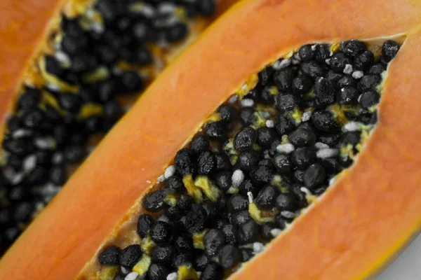 Half cut ripe papaya with seed on a white plate. Slices of sweet papaya with a white background. Halved papayas. Healthy exotic fruits. Vegetarian food.