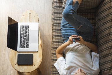 Bir kadın kanepede dizüstü bilgisayar ve masada kitap okurken akıllı telefon kullanır. Çevrimiçi çalışma, serbest çalışma. Serbest çalışan ya da serbest çalışan bir kız telefonunu kullan ve işten izin al..