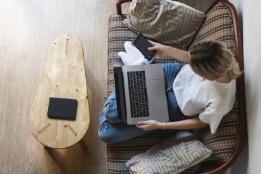 Dizüstü bilgisayarı olan bir kadın kanepede oturuyor ve akıllı telefon kullanıyor. İnternette çalış ve çalış, serbest çalış. Serbest meslek sahibi bir kız defteriyle çalışıyor. Masasında telefon ve okuyucusuyla bir kanepede oturuyor..