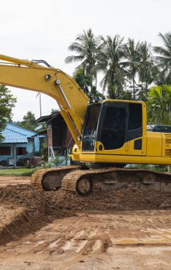 Mavi gökyüzüne karşı bir inşaat alanında sarı kazıcı. Ağır endüstri. Endüstriyel kazıcının detaylarını kapat. Arka planda avuç içleri olan turuncu bir zeminde duran büyük bir iz kazıcı..