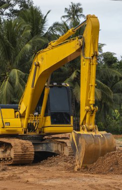 Mavi gökyüzüne karşı bir inşaat alanında sarı kazıcı. Ağır endüstri. Endüstriyel kazıcının detaylarını kapat. Arka planda avuç içleri olan turuncu bir zeminde duran büyük bir iz kazıcı..