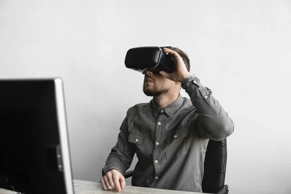 Jovem barbudo sentado contra computador com óculos de realidade virtual. Tecnologias modernas. O conceito de tecnologia futura . — Fotografia de Stock