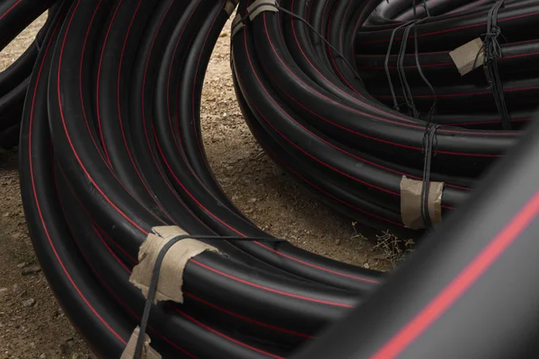 Tuyaux noirs en caoutchouc ou en plastique avec des lignes rouges comme matériau de construction et équipement sur le chantier. Utilisation comme tuyau d'eau . — Photo