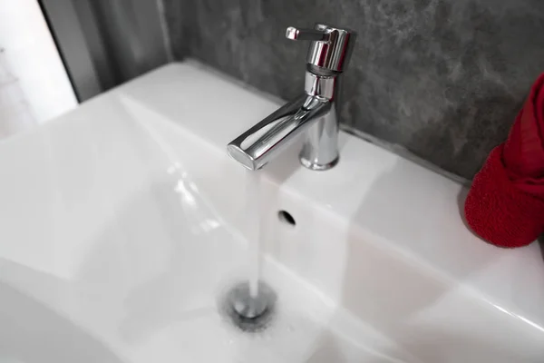 Eau courante du robinet moderne en acier inoxydable dans un évier blanc. Comptoir salle de bain intérieur contemporain. Salle de bain design luxueuse et élégante avec des murs en béton . — Photo