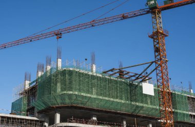 Mavi gökyüzüne karşı vinç ve inşaat alanı. İnşaatın bitmemiş binasının metal inşaatı. Crane kulesi çok katlı depo inşaatı için kullanılıyor.