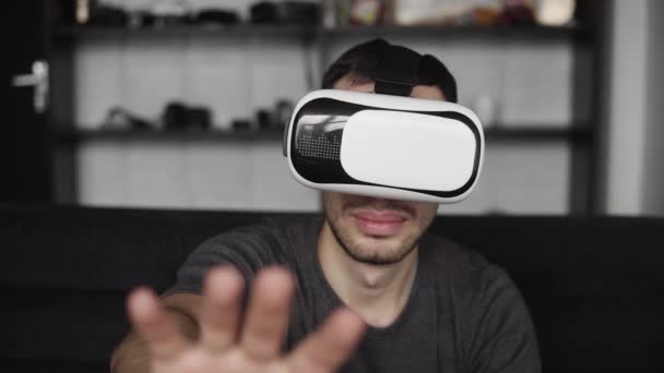 Ung bearded man bär headsetet av virtuell verklighet i kontor sitter på en soffa och försökte röra något som han ser i virtuella världen. — Stockvideo