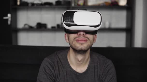 ソファに座ってオフィスで仮想現実のヘッドセットを身に着けている若い髭の男。VRの世界と彼がヘッドセットで見たものを探索する. — ストック動画