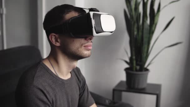 Young bearded man wearing headset of virtual reality in office sitting on a sofa. Exploring VR world and all what he saw in headset. — 비디오