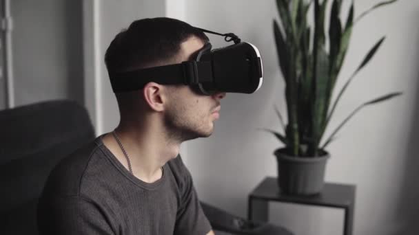 Young bearded man wearing headset of virtual reality in office sitting on a sofa. Exploring VR world and all what he saw in headset. — Stock Video