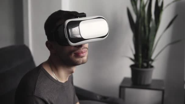 Young bearded man wearing headset of virtual reality in office sitting on a sofa and trying to touch something that he see in virtual world. — Stock Video