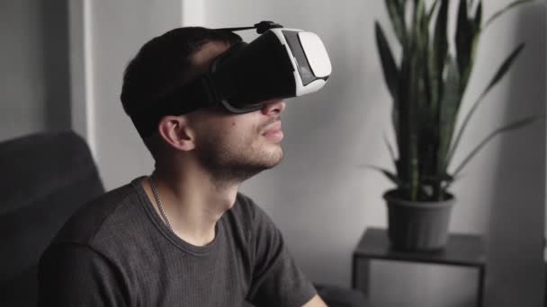 Mladý vousatý muž ve sluchátkách virtuální reality sedí na pohovce. Zkoumání Vr světa a všeho, co viděl ve sluchátkách. — Stock video