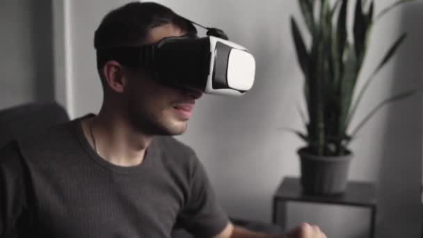 Fiatal szakállas férfi visel headset virtuális valóság az irodában ül egy kanapén, és tánc. — Stock videók