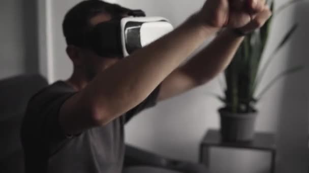 Jonge man met baard draagt een headset van virtual reality op kantoor zittend op een bank en dansend. — Stockvideo