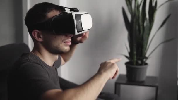 Giovane uomo barbuto che indossa cuffie di realtà virtuale in ufficio seduto su un divano e ballare . — Video Stock