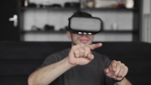 Jovem barbudo vestindo fone de ouvido de realidade virtual no escritório sentado em um sofá e tentando tocar algo que ele vê no mundo virtual. Usando fone de ouvido VR para o trabalho . — Vídeo de Stock