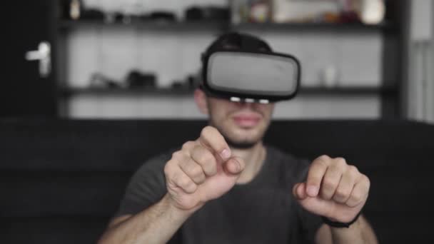 Jonge man met een baard draagt een headset van virtual reality op kantoor zittend op een bank en probeert iets aan te raken wat hij in de virtuele wereld ziet. Gebruik van Vr-headset voor werk. — Stockvideo