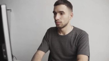 Genç işadamı öğrenci ya da gömlekli serbest çalışan bilgisayar monitörüne karşı oturan ve ofisteki bir masada düşünceli bir ifadeyle klavye yazan biri. Ofiste dizüstü bilgisayarı üzerinde çalışıyor..