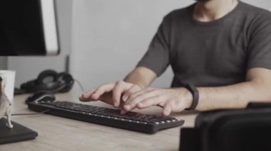 İş adamı öğrenci ya da tişörtlü serbest çalışan bilgisayar monitörüne karşı oturan ve ofisteki bir masada klavye yazan biri. Ofiste dizüstü bilgisayarı üzerinde çalışıyor..